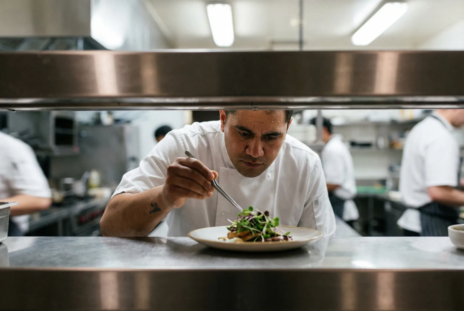 A chef plating a dish on the pass in a commercial kitchen.